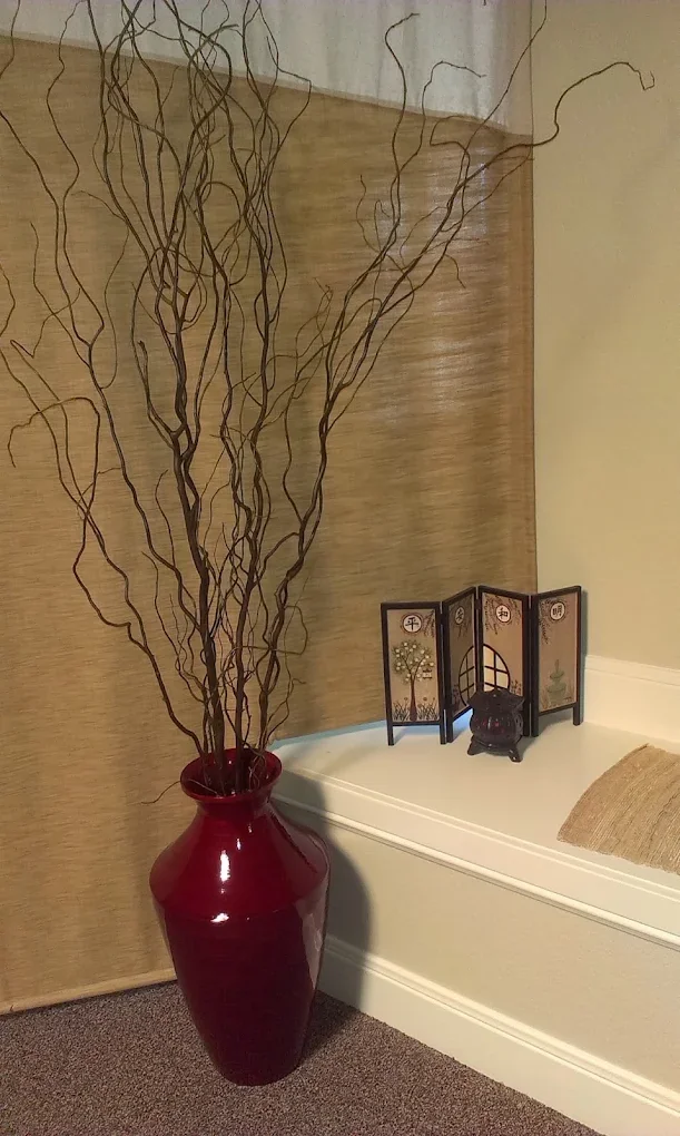Natural branches in a burgundy vase beside the studio’s tan privacy curtain
